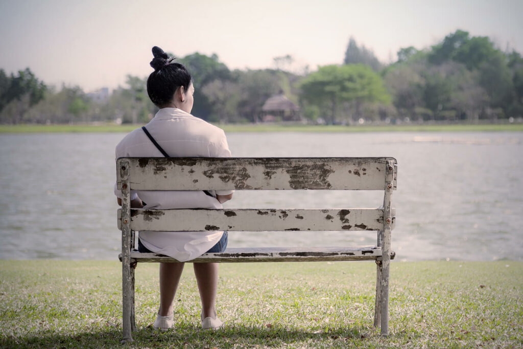 A woman sitting on a bench near the water contemplating life. If your life has become a struggle due to trauma, EMDR Therapy in Washington, DC can help.
