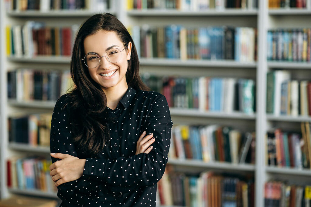 Young college student smiling with shelves of books in the background representing someone who has learned to harness the power of ADHD through ADHD Therapy for Adults in Washington, DC.