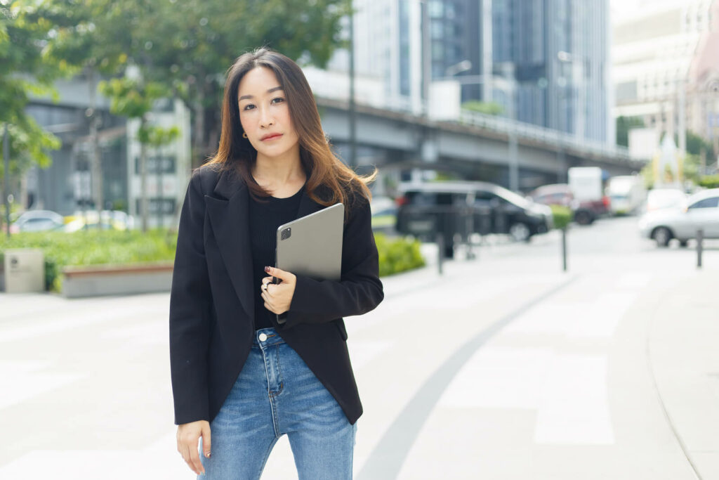 Young Asian professional woman standing with her laptop looking despondant representing her battle with ADHD aas an urban professiona;. ADHD Therapy for Adults in Washington, DC can help you regain focus and control.