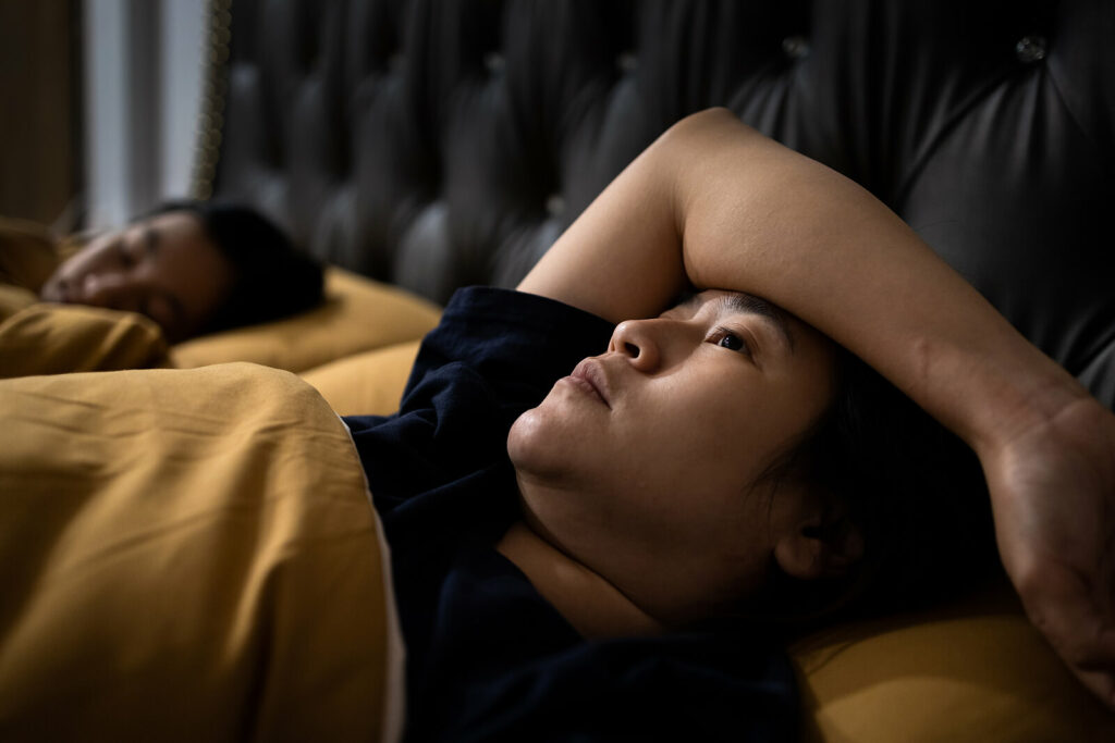 An Asian woman lies in bed staring at the ceiling as she struggles with her anxiety. EMDR Therapy in Washington, DC can help you overcome your anxiety and depression.