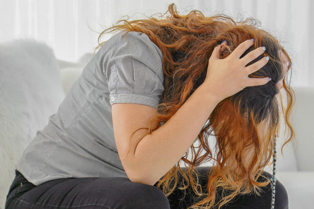 A red headed woman sits with her head in her hands as she struggles to overcome feelings of depression. Depression Treatment in Washington, DC is available to help.