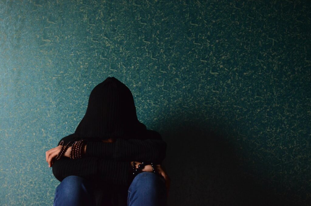 An individual sits with their arms crossed over their knees as they lean against a wall representing someone who could benefit from Therapy for Depression in Washington, DC.