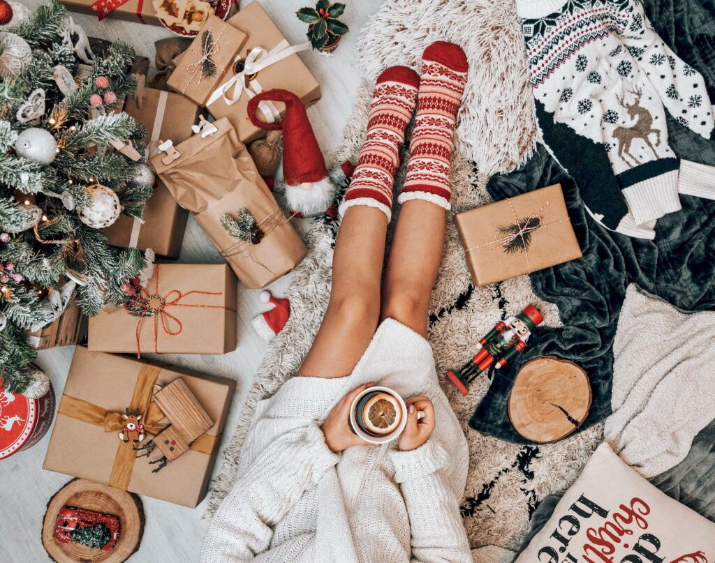 A woman sets on a rug with a cup of tea surrounded by gifts and Christmas decor representing the chaos of the season. Combat holiday anxiety in Anxiety Therapy in Washington, DC.