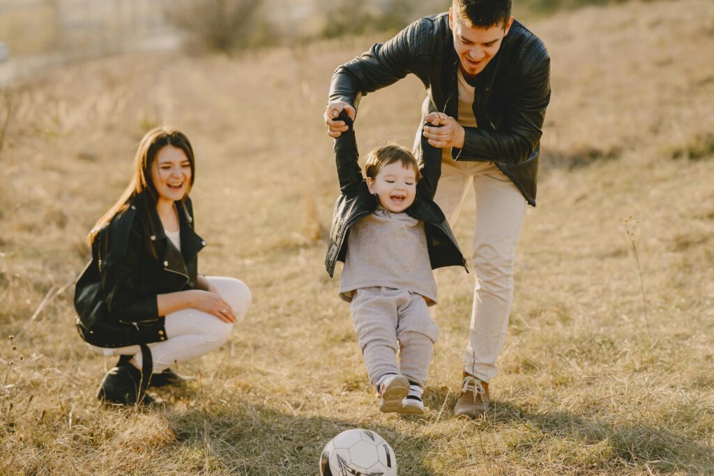 A dad helps his son kick a ball while mom looks on smiling. Let Depression Therapy in Washington, DC help you improve your parenting skills!
