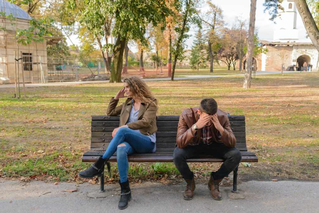 Woman And Man Sitting on Brown Wooden Bench looking visibly upset