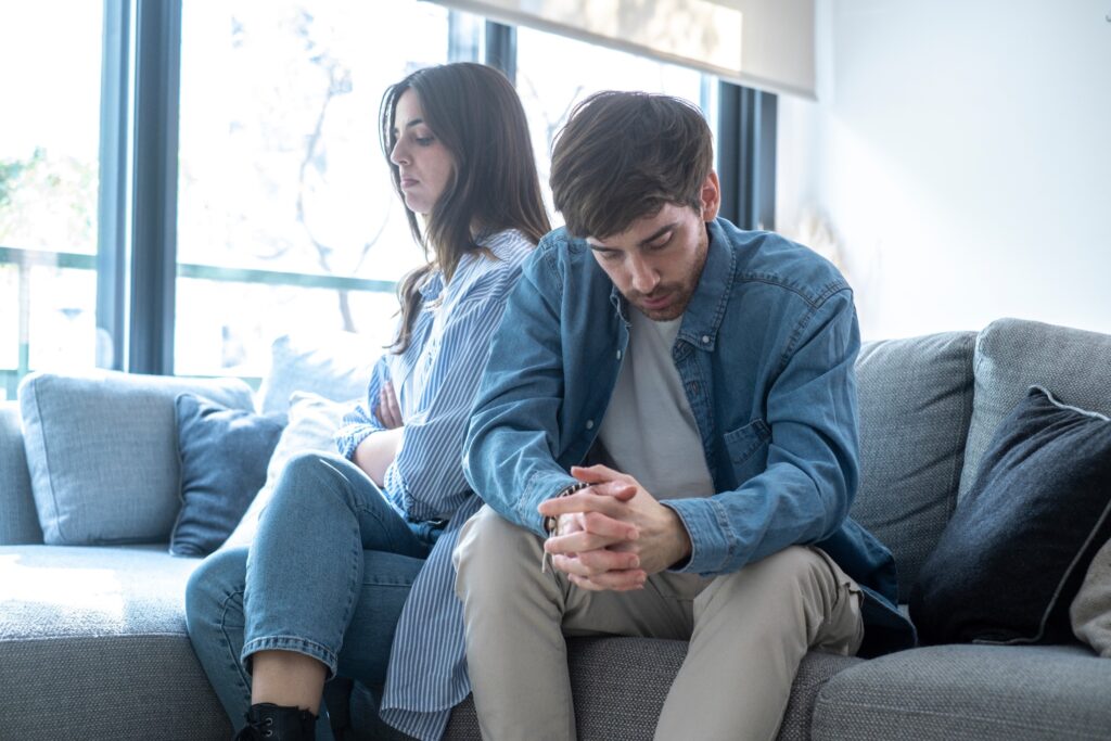 Couple sitting apart on couch looking distressed and disconnected, showing relationship communication difficulties