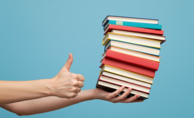 Person giving thumbs up while holding colorful stack of books for ADHD and trauma recovery recommendations