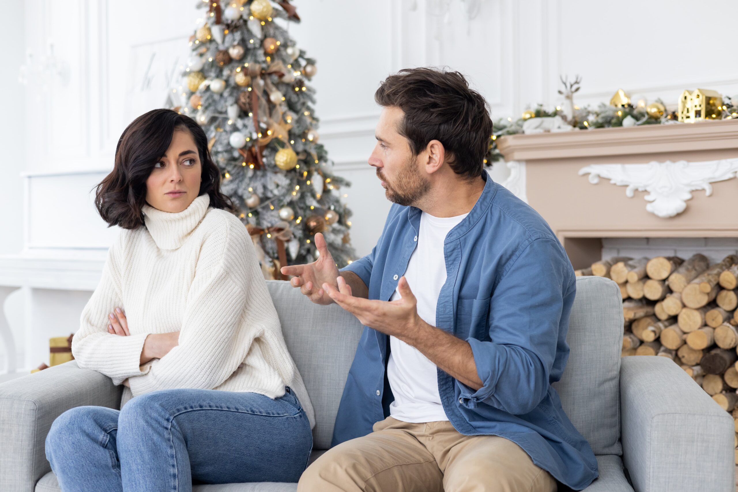 Couple having difficult conversation on couch with Christmas tree, showing how ADHD couples struggle during the holidays with communication and stress