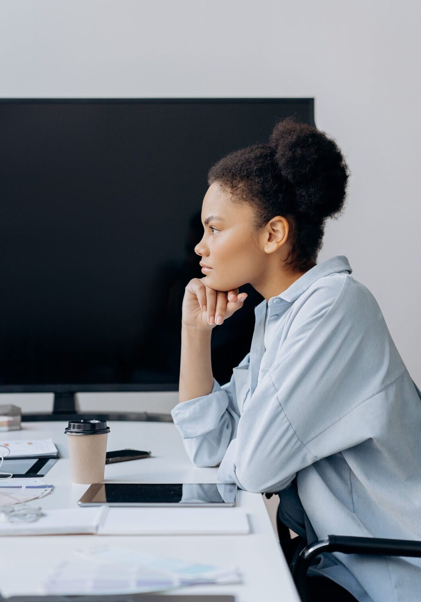 Woman resting her chin on her hand, looking off thoughtfully at her desk